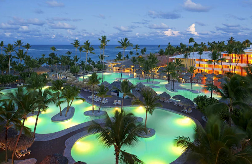Vista aérea cenital del resort Iberostar Waves Punta Cana en Playa Bávaro, República Dominicana, mostrando el mar turquesa, las piscinas de diseño curvo y los jardines con palmeras