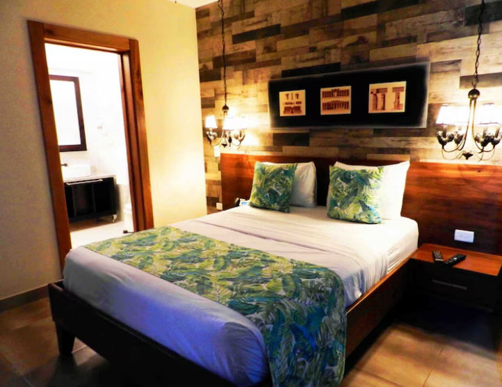 Recepción de Mon Boutique Hotel en Constanza con una recepcionista sonriendo detrás de un mostrador rústico de madera recuperada, pared de piedra y un letrero dorado ovalado de cuatro estrellas iluminado por una lámpara industrial