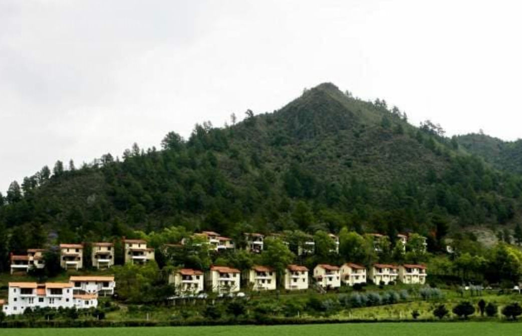 Cabañas rústicas de color beige en Alto Cerro Villas Hotel Camping rodeadas de vegetación y flores de color rojo anaranjado con montañas al fondo