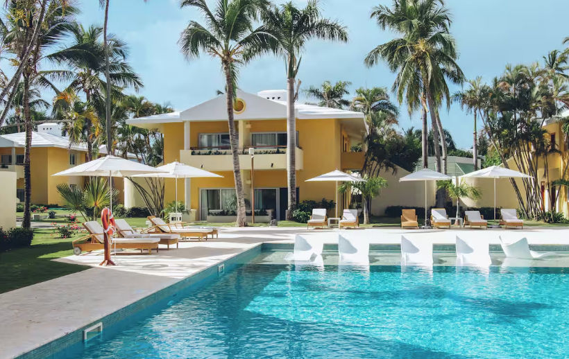 Piscina infinita frente a la playa en un resort de lujo en Punta Cana con tumbonas, sombrillas y palmeras