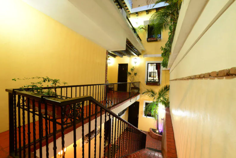Fachada exterior iluminada de noche de un restaurante de estilo colonial con paredes blancas, ventanas con rejas de hierro, plantas decorativas y luces cálidas en la entrada
