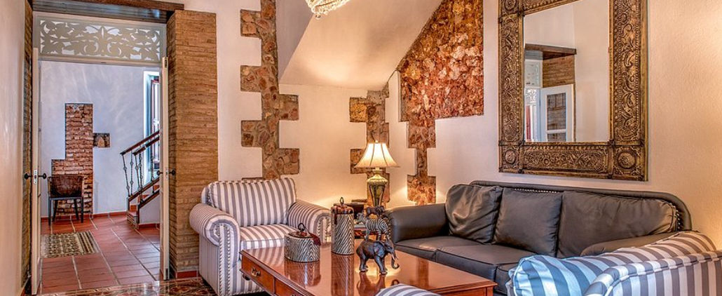 Interior del hotel Colonial 154 H Boutique en Santo Domingo, sala de estar con paredes de piedra rústica, sofás elegantes y decoración colonial - Interior of Colonial 154 H Boutique hotel in Santo Domingo, living room with rustic stone walls, elegant sofas, and colonial decor