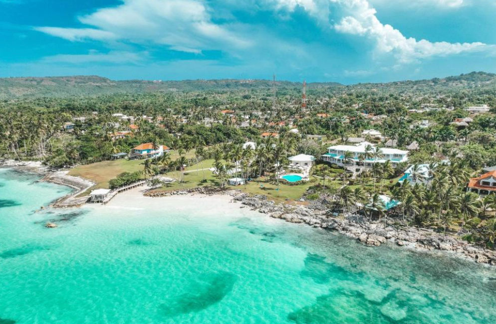 Panoramic view of Villa Serena in Las Galeras featuring a curved swimming pool, tropical palm tree garden, and white sand beach facing the ocean