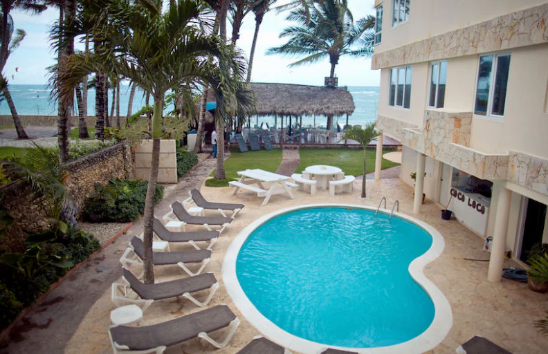 Exterior facade of the Kite Beach Inn hotel in Cabarete, featuring parked vehicles in front, a wind turbine, and a clear blue sky