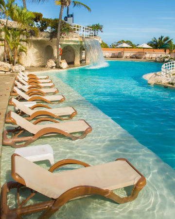 Vista aérea de las piscinas de Cofresi Palm Beach y Spa Resort rodeadas de palmeras con el océano Atlántico al fondo