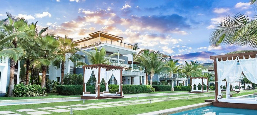Exterior view of luxury wooden cabanas with white curtains at Sublime Samana Hotel Residences with green mountains in the background