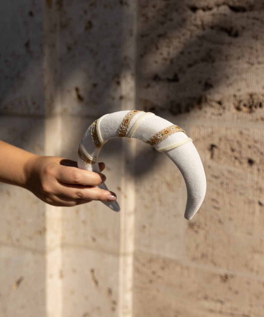 A woman's hand holding a WALD Berlin Headband Swirl White in front of a stone wall.