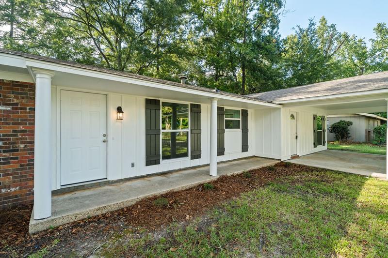 Covered front porch with white columns, dark shutters, and an adjoining carport