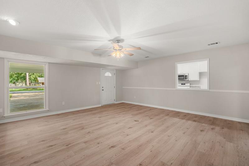 Living room with a kitchen pass-through, large window, and ceiling fan