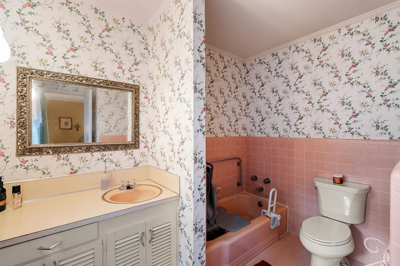 Primary bath with original pink tile and floral wallpaper