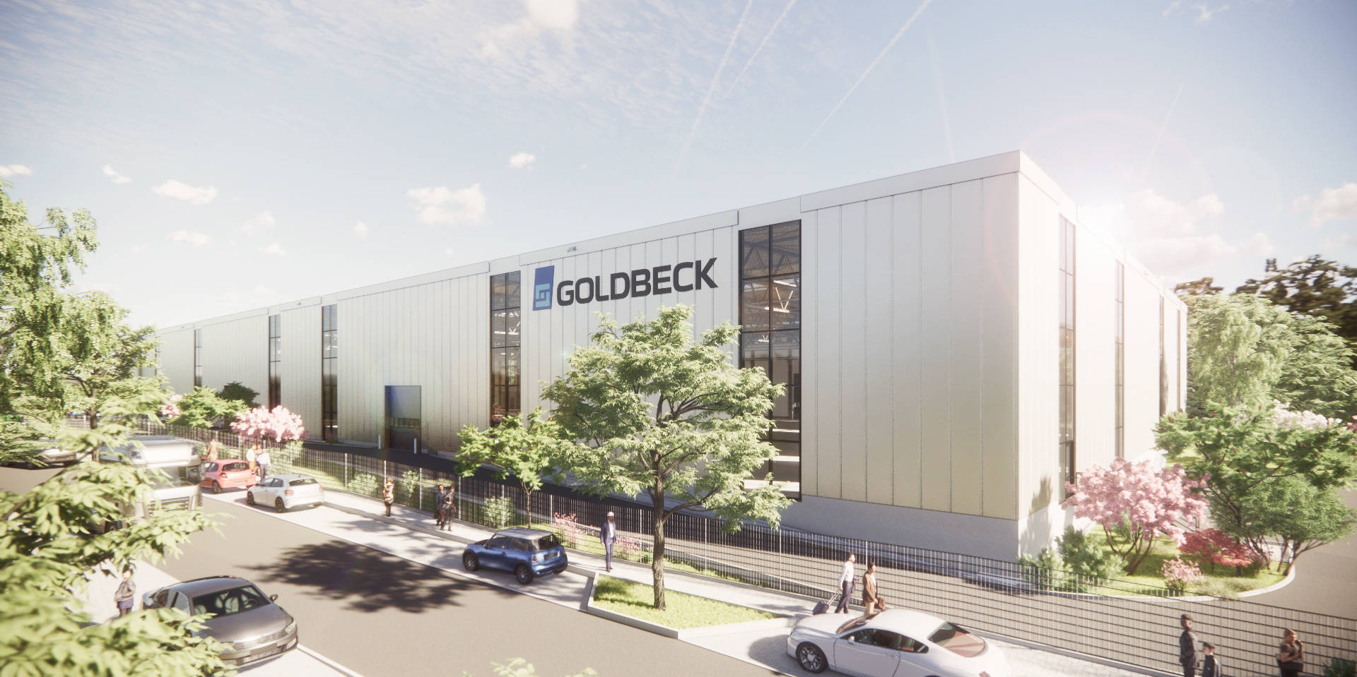 Moderne Industriehalle mit Goldbeck-Logo, umgeben von Bäumen und vorbeifahrenden Autos bei Tageslicht.