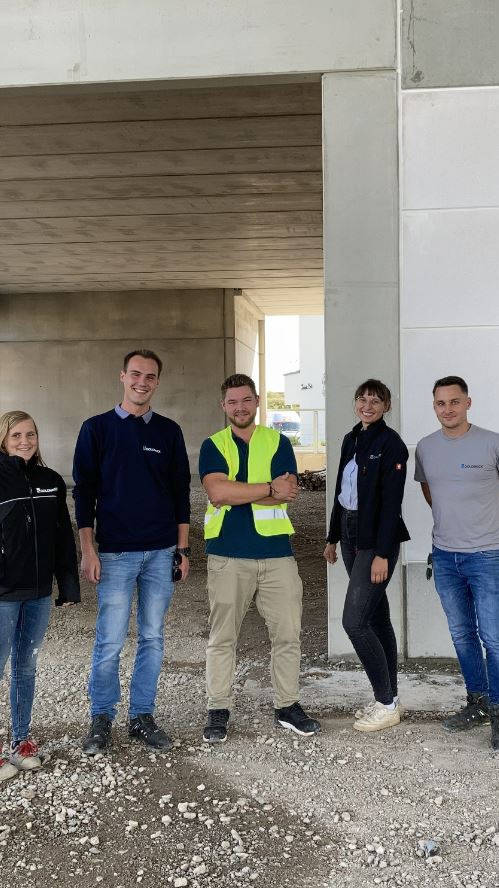 Fünf Personen, die in Freizeitkleidung und einer Warnweste auf einer Baustelle posieren.