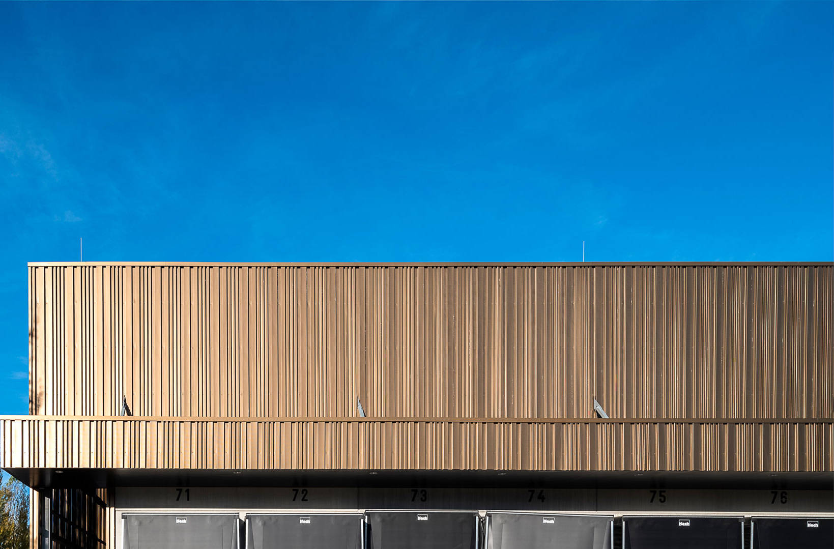 Warehouse with loading ramps and a yellow postal truck parked in a parking lot under a clear sky.