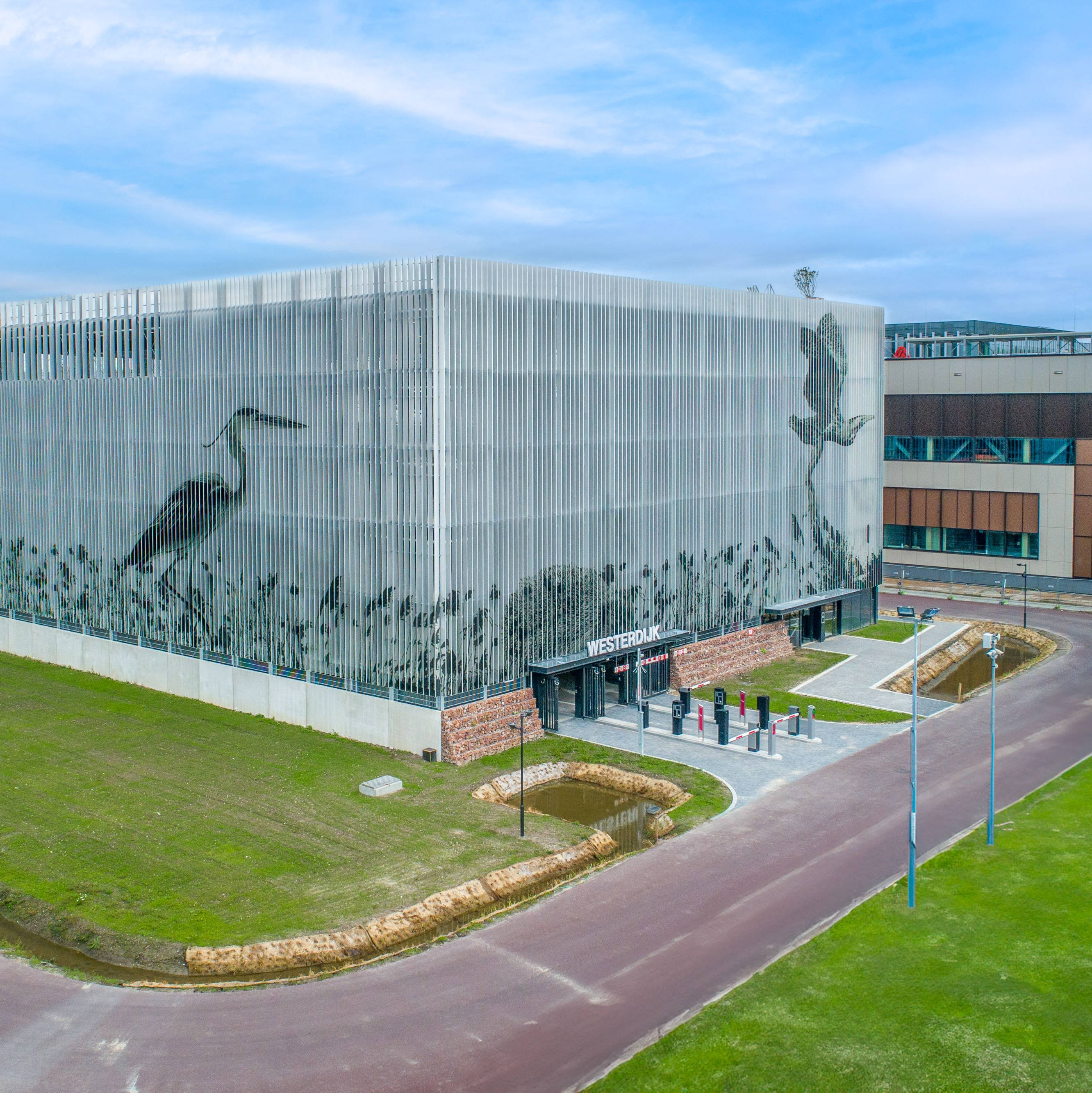 Een modern gebouw met een groot raster waarin afbeeldingen van vogels en planten zijn verwerkt. Boven de ingang staat "Westerdijk". Het gebouw staat op een terrein met gras en een verharde weg eromheen.
