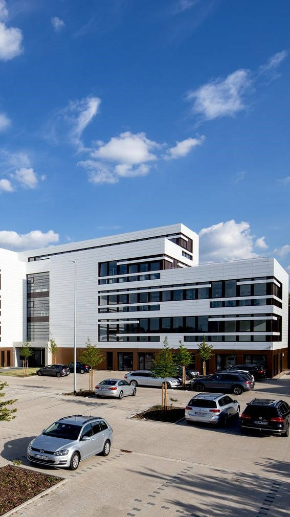Modern office building with white facades and adjacent parking lot under a blue sky.