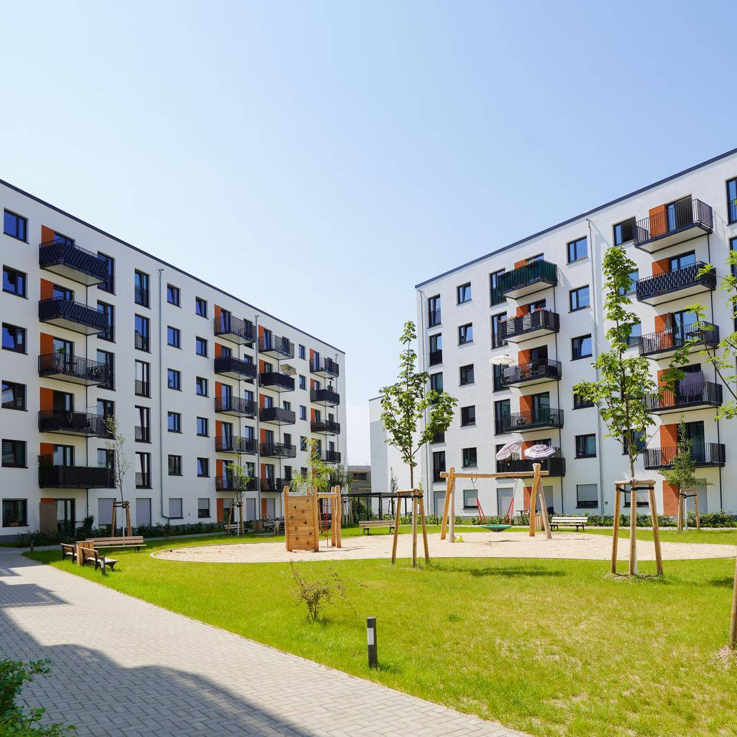 Modern residential complex with several apartments, inner courtyard with lawn, young trees and playground.