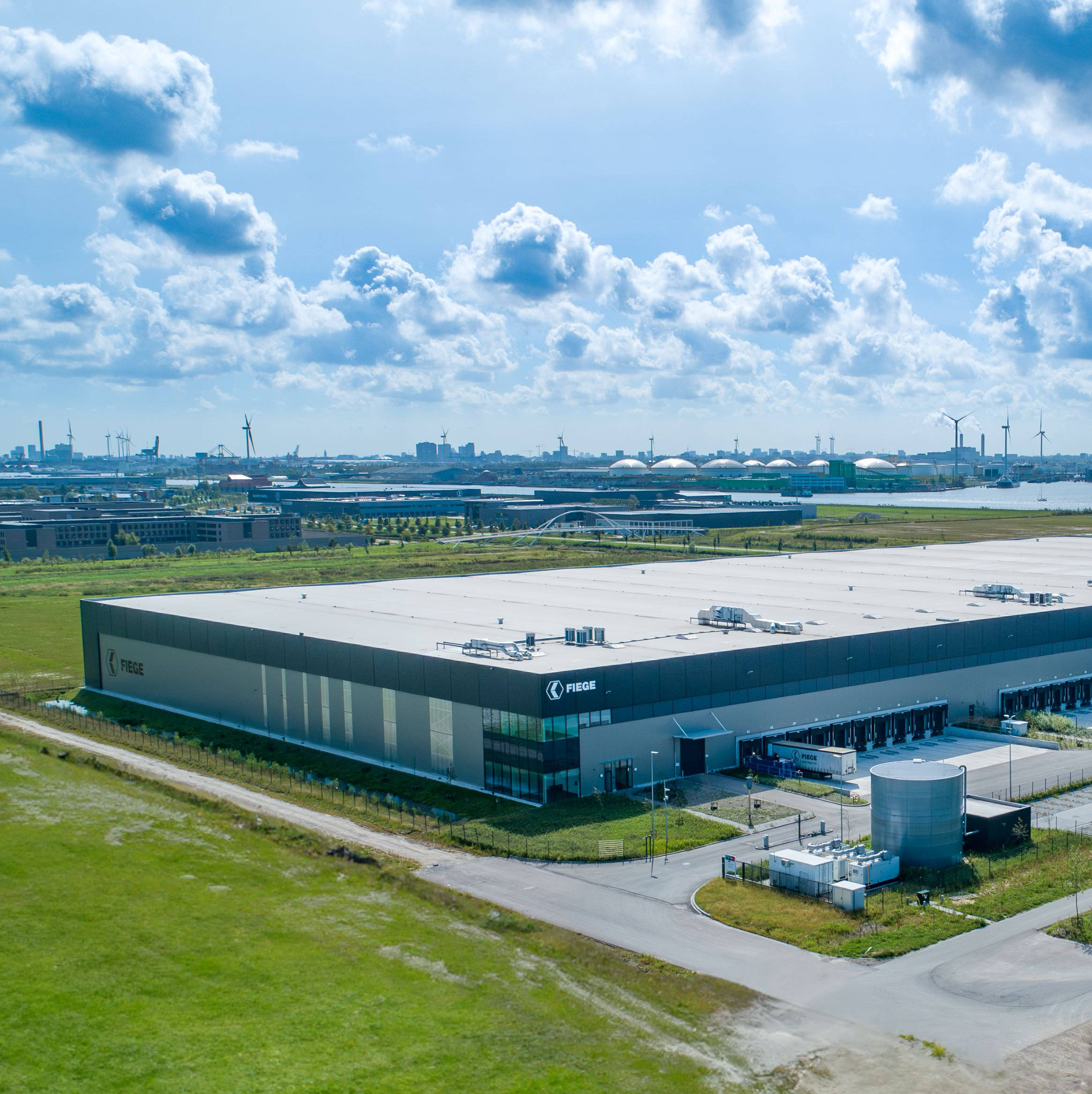 Ingang van een parkeergarage met de tekst "WESTERDIJK" erboven, met slagbomen, torenhoge metalen hekwerken en een stenen muur aan de zijkant. The ground around it is grassy.