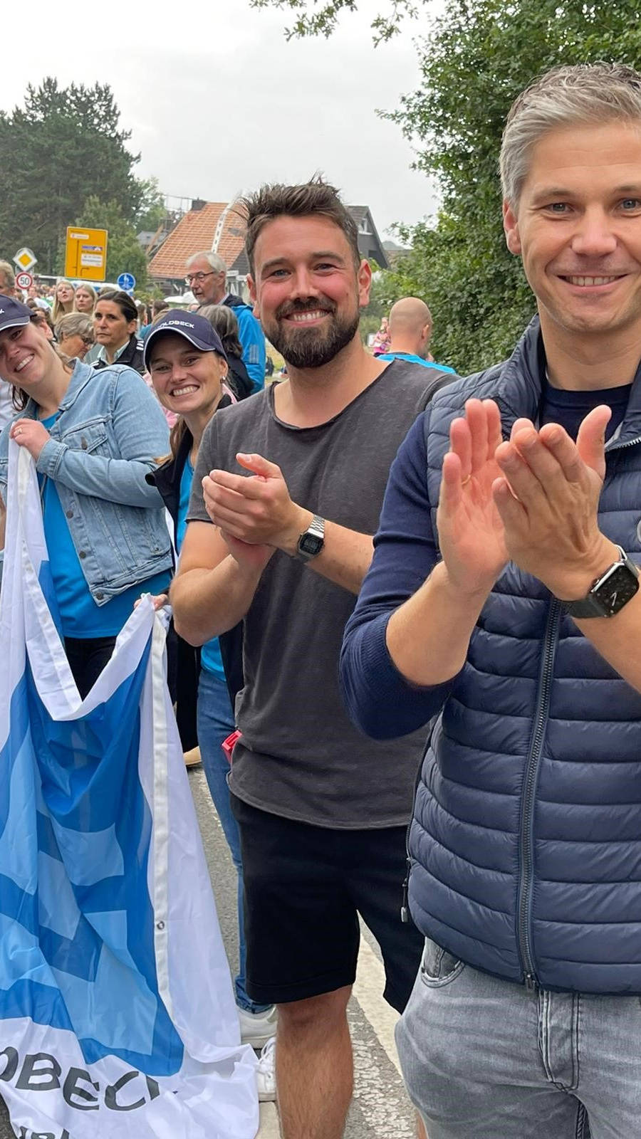 Leute klatschen am Straßenrand eines Marathons, halten ein Banner und freuen sich über die vorbeilaufenden Teilnehmer.