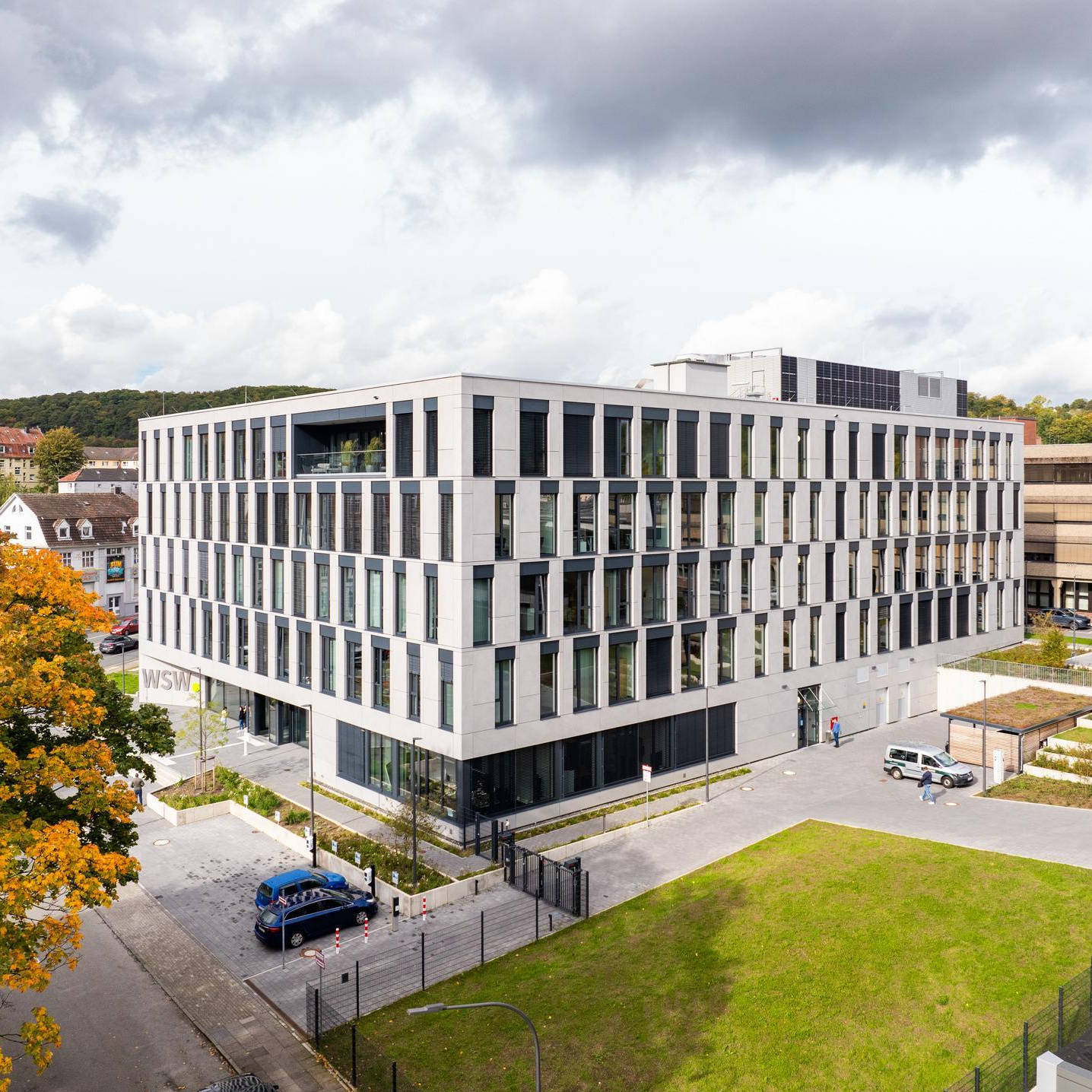 Modernes Bürogebäude mit großen Fenstern, umgeben von grünen Flächen und einer Straße, im Herbst.