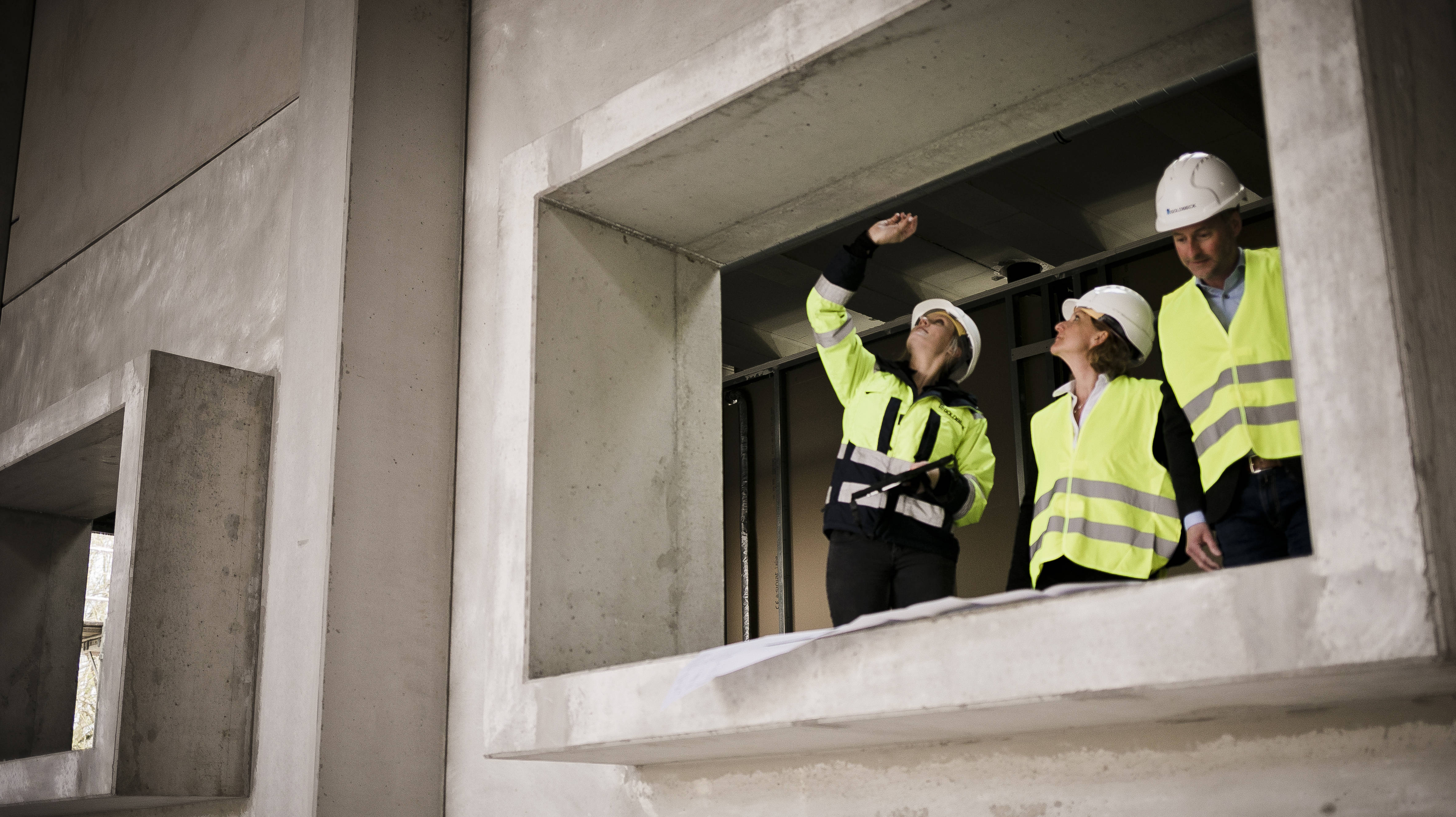 Drei Bauingenieure in Schutzwesten und Helmen begutachten eine Betonstruktur von innen.
