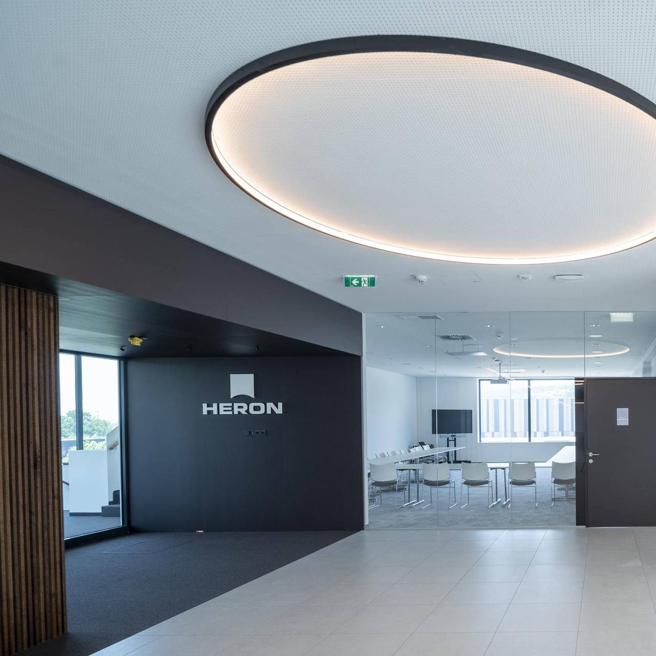 Modernes Bürointerieur mit Glaswänden, Konferenzraum und stilvoller Beleuchtung. Logo "HERON" an einer Wand.