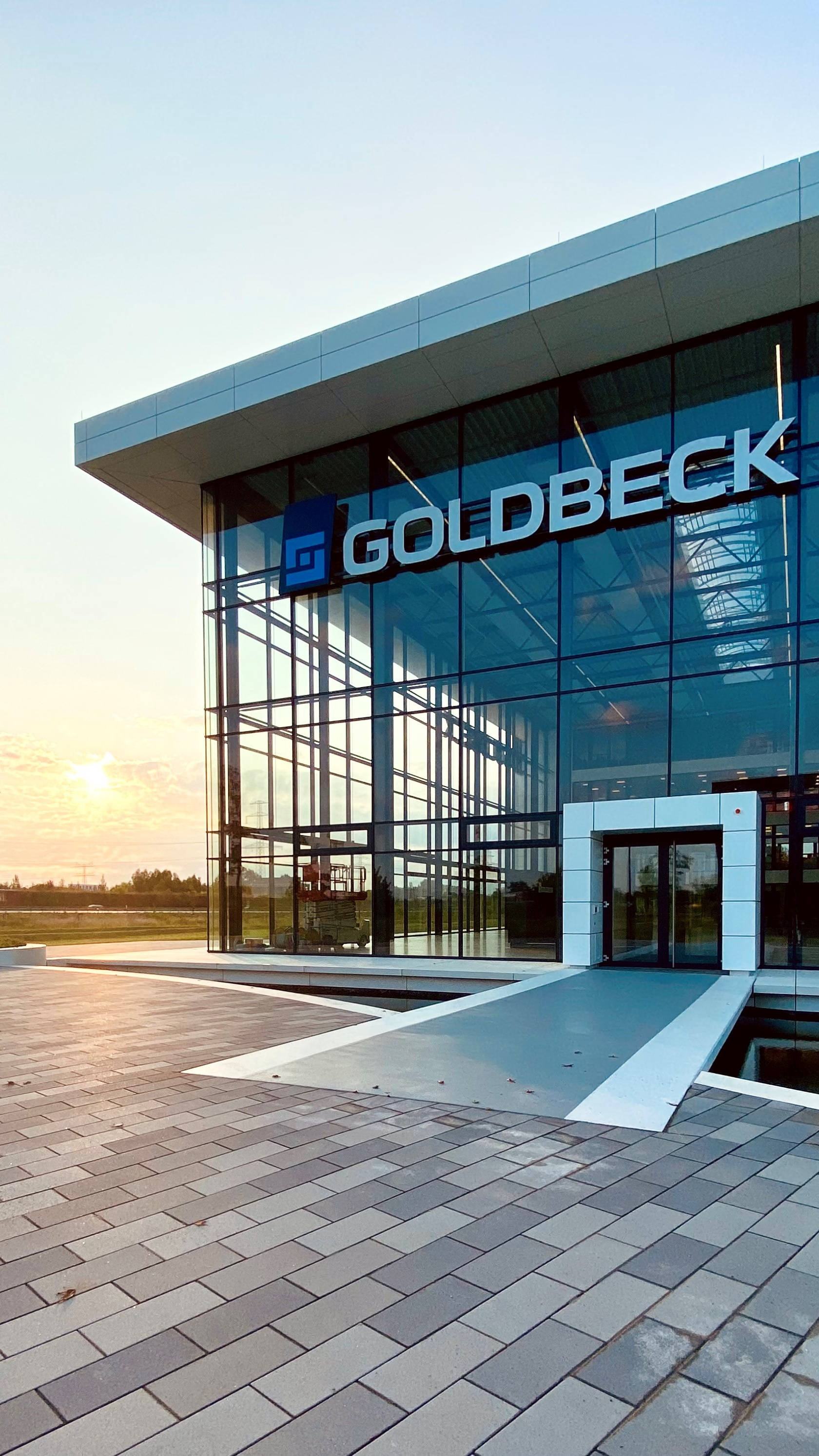 Modernes Bürogebäude mit Glasfassade und Goldbeck-Logo, beleuchtet durch Abendsonne.