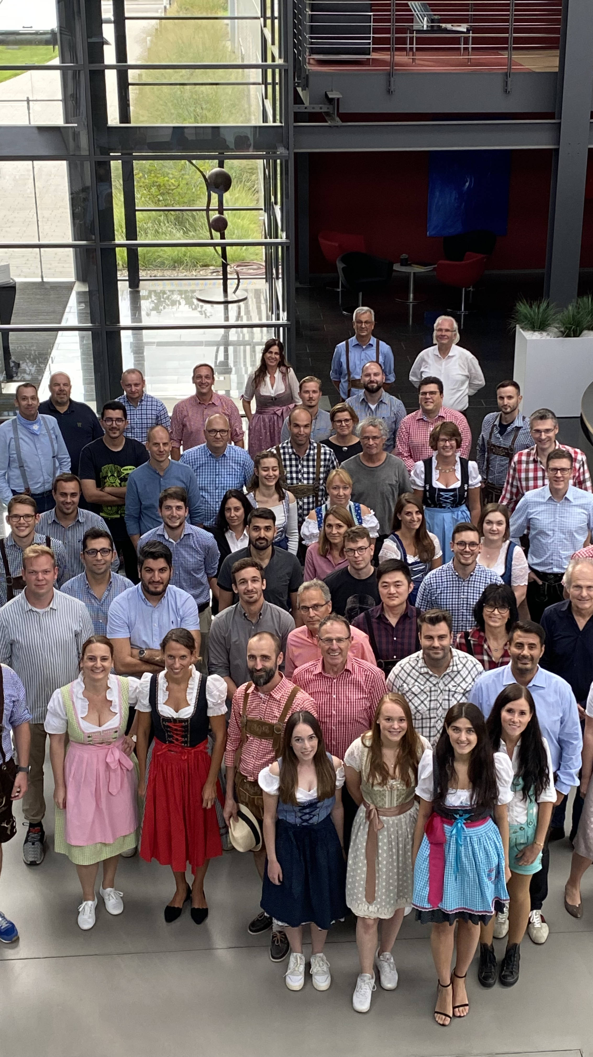 Eine große Gruppe von Menschen in traditioneller bayerischer Tracht und Alltagskleidung steht in einem modernen Firmengebäude.