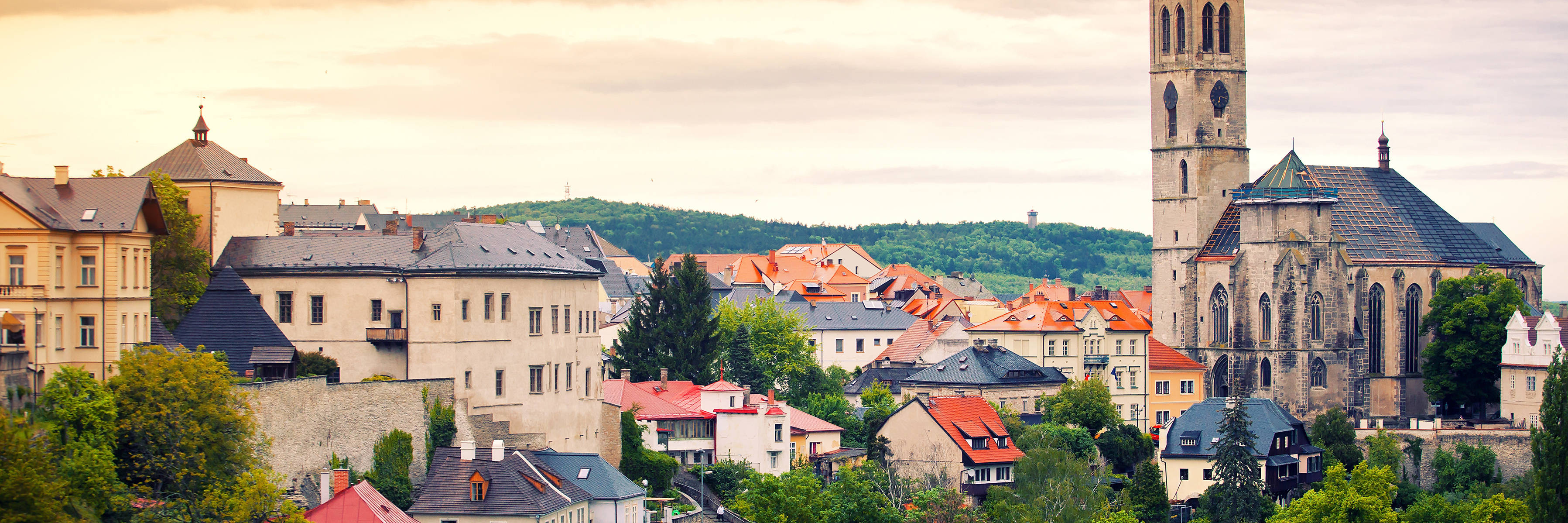 Pohled na středověké město Vrdy s kostelem a barevnými domy při západu slunce, obklopené zelenými kopci.