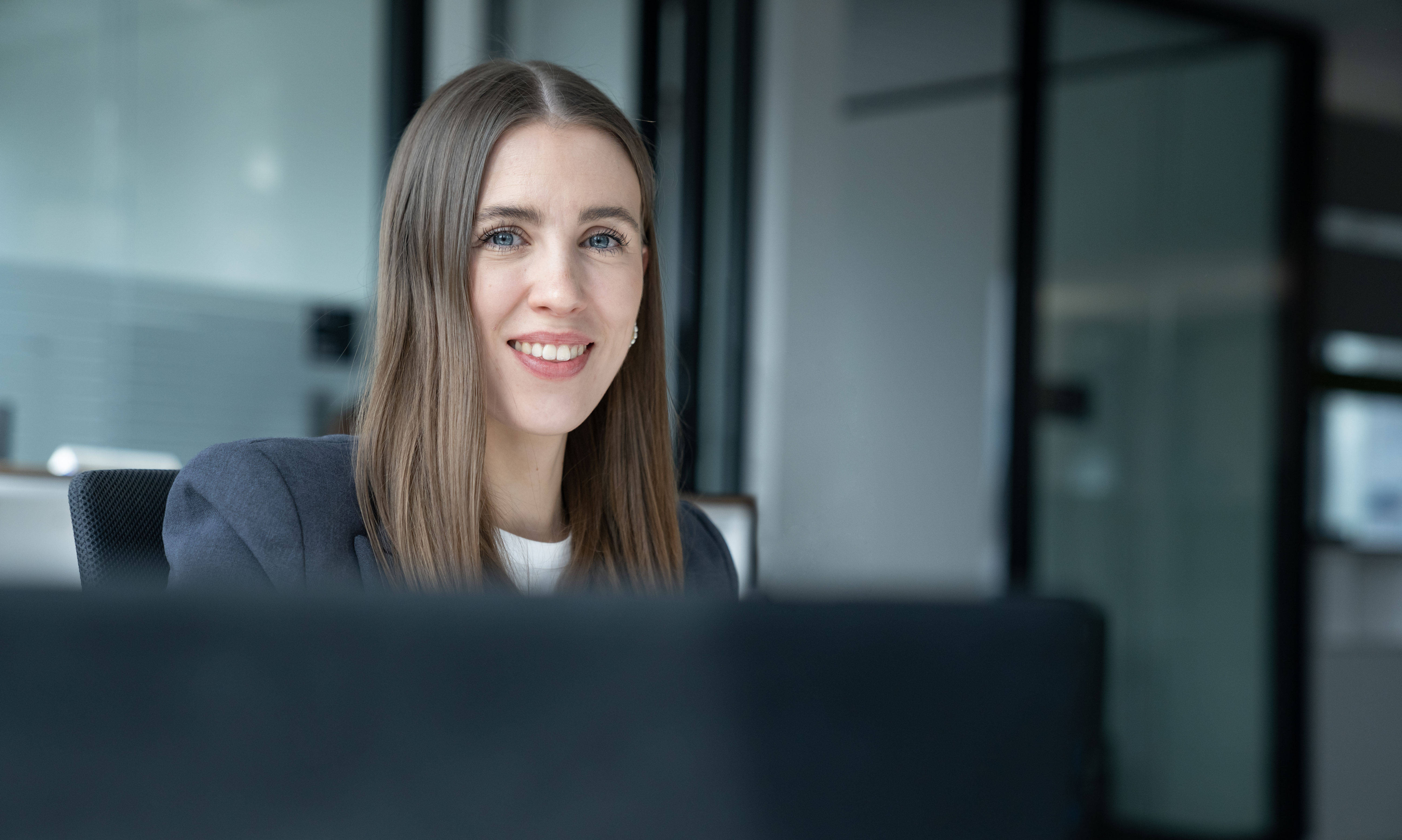 Lächelnde Frau in einem modernen Büro mit Glaswänden im Hintergrund.