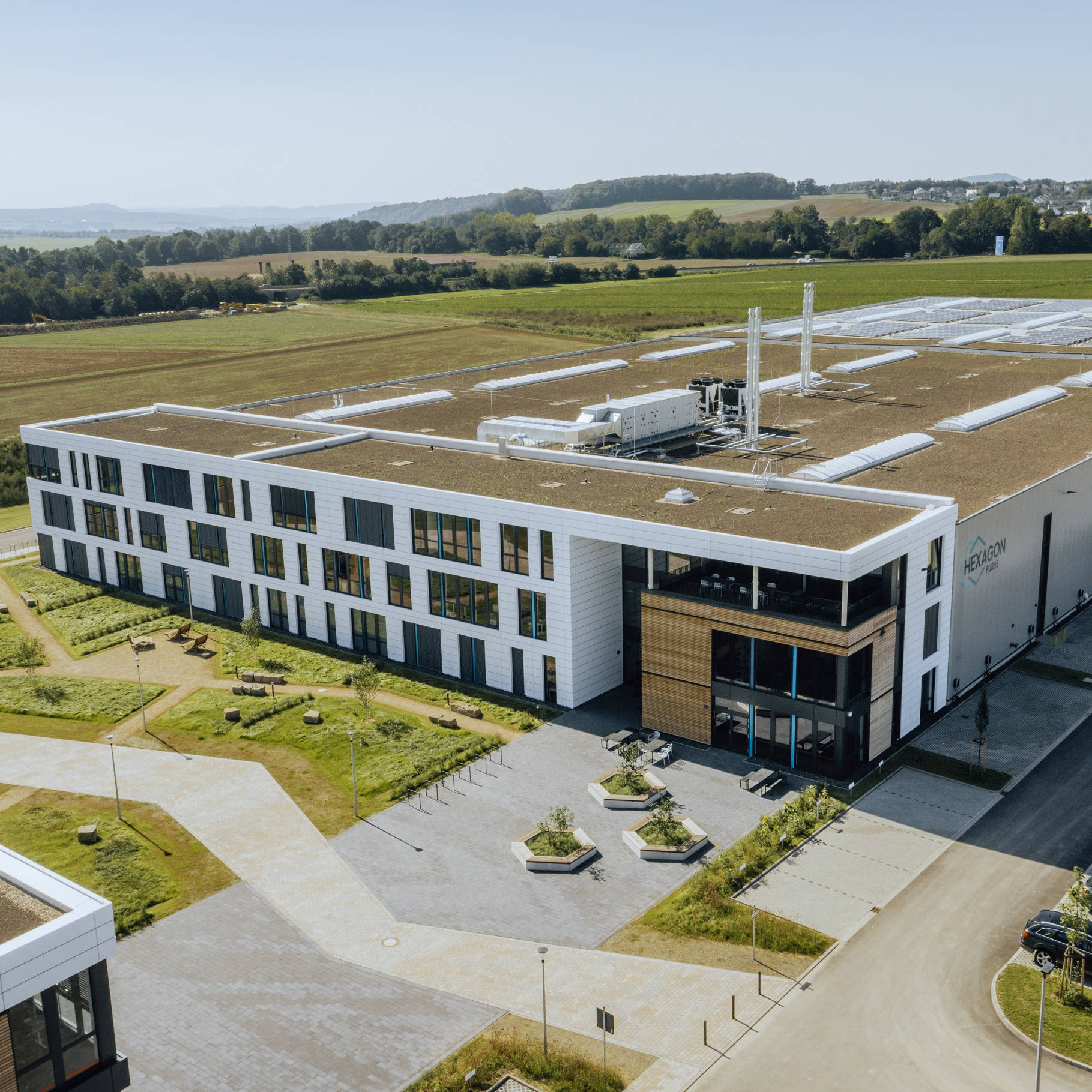 Modernes Industriegebäude mit bepflanztem Dach und Solarpanels, umgeben von ländlicher Landschaft.
