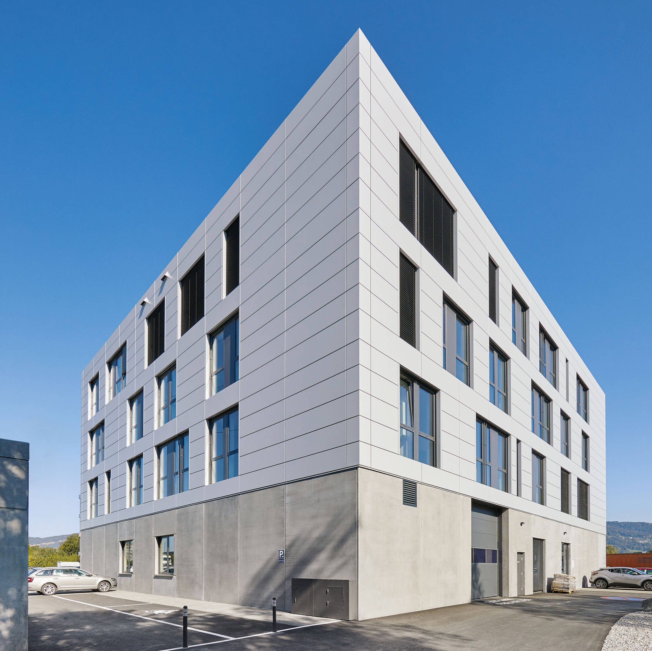 Modernes fünfstöckiges Bürogebäude mit Glasfront und weißer Fassade unter blauem Himmel.