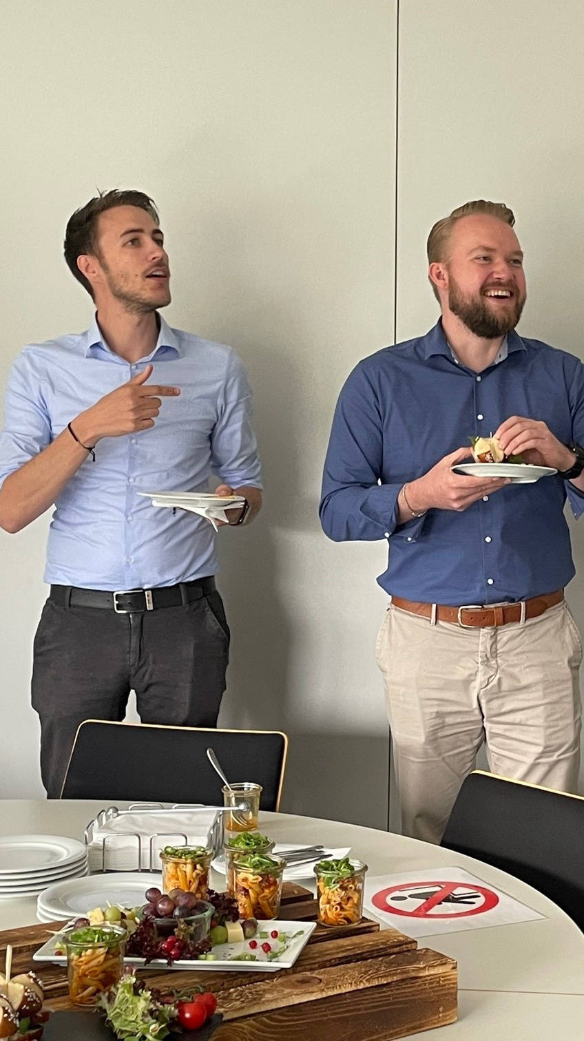 Personengruppe unterhält sich bei einem Bürosnack am Tisch mit Obst und kleinen Gerichten.