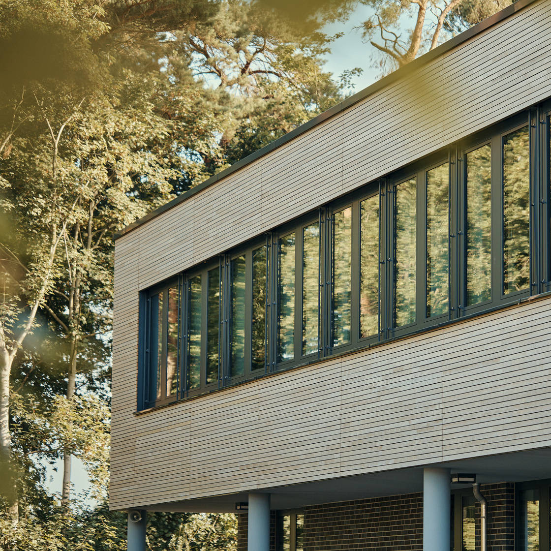 Modern glass façade of a building with reflection of trees and sky.