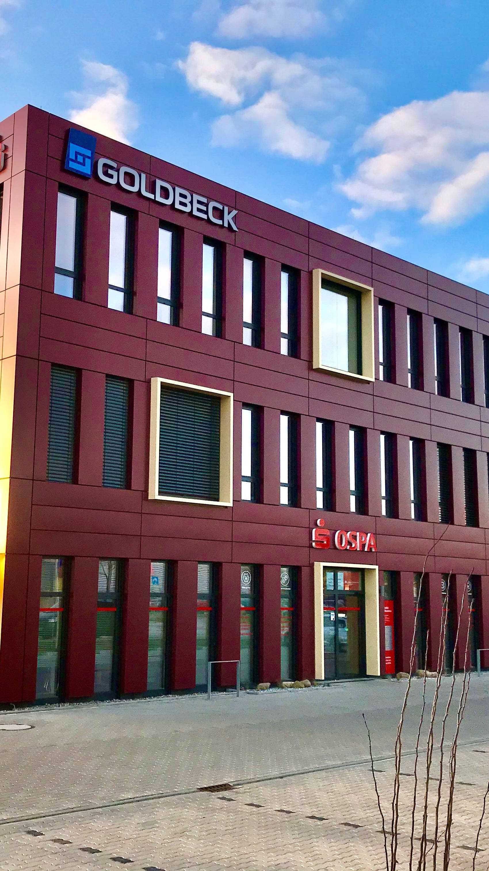 Moderner Bürogebäudekomplex mit roten Fassaden und großen Fenstern unter blauem Himmel, Logos von Firmen auf der Fassade.