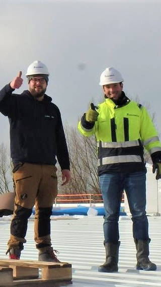 Zwei Bauarbeiter in Schutzkleidung und Helmen geben Daumen hoch auf einer Baustelle.