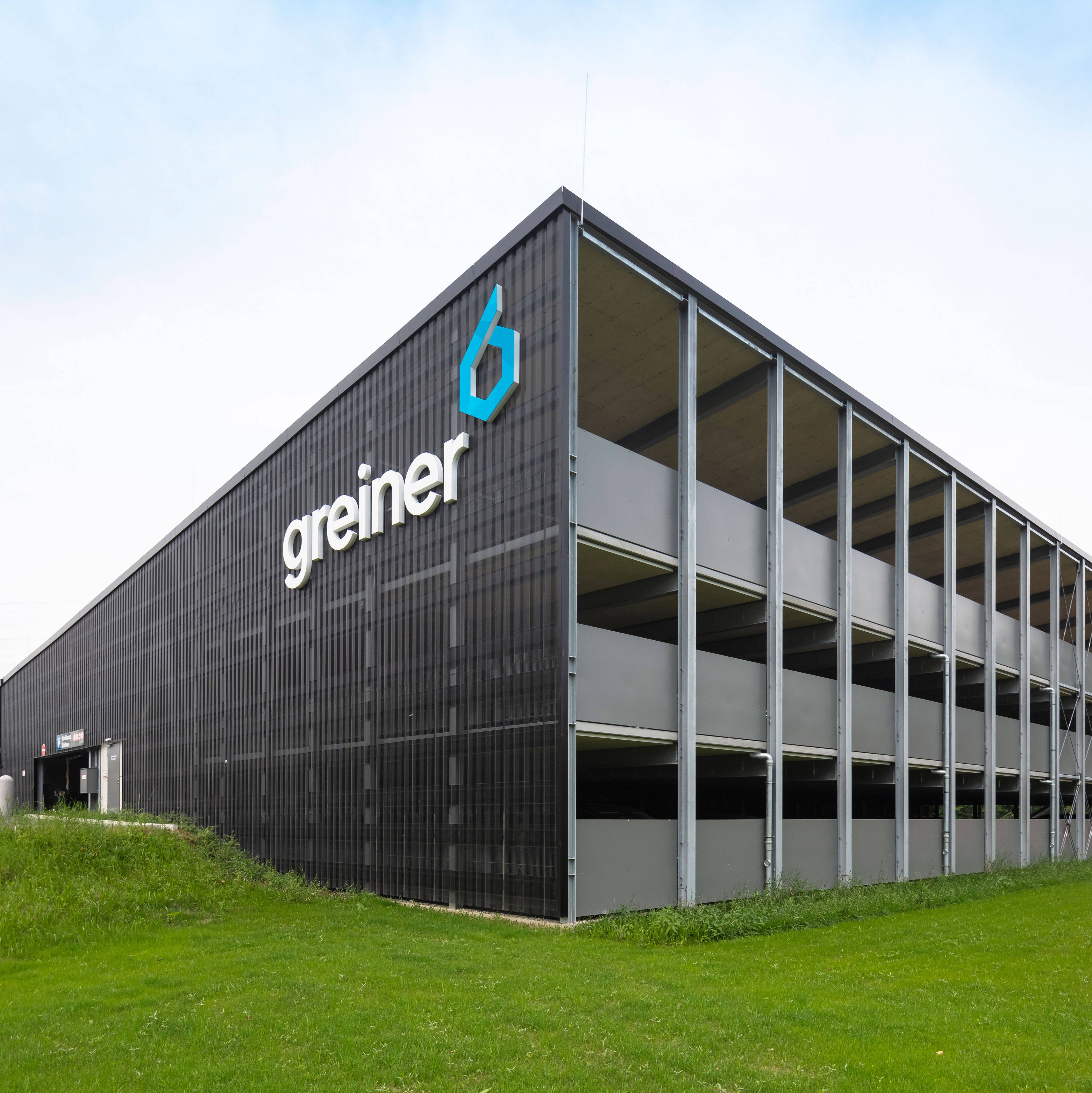 Mehrstöckiges Parkhaus mit dem Logo von Greiner an der Fassade, umgeben von Rasenflächen.