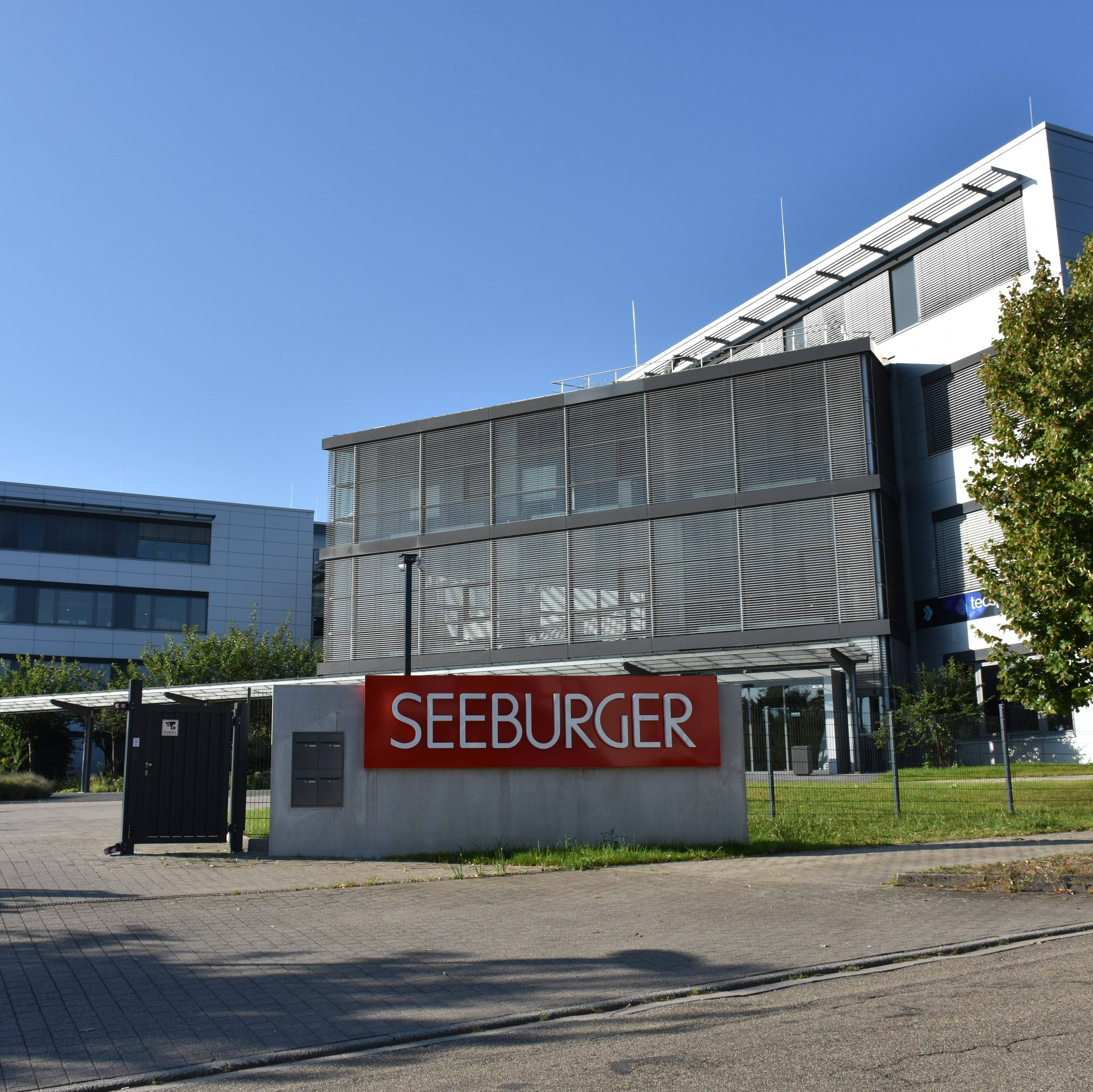 Modernes Bürogebäude mit der Aufschrift "SEEBURGER" auf einem Schild. Blauer Himmel im Hintergrund.