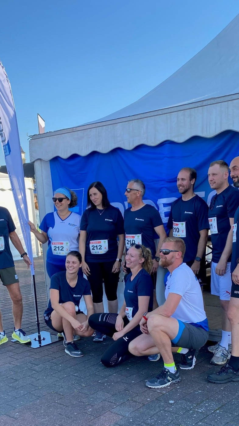 Gruppe von Menschen in Sportkleidung mit Startnummern posiert vor einem Zelt bei einer Laufveranstaltung.