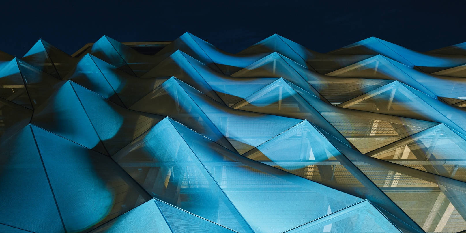 Futuristic blue façade of the Schüco parking garage with triangular structures against the night sky, modern architecture.