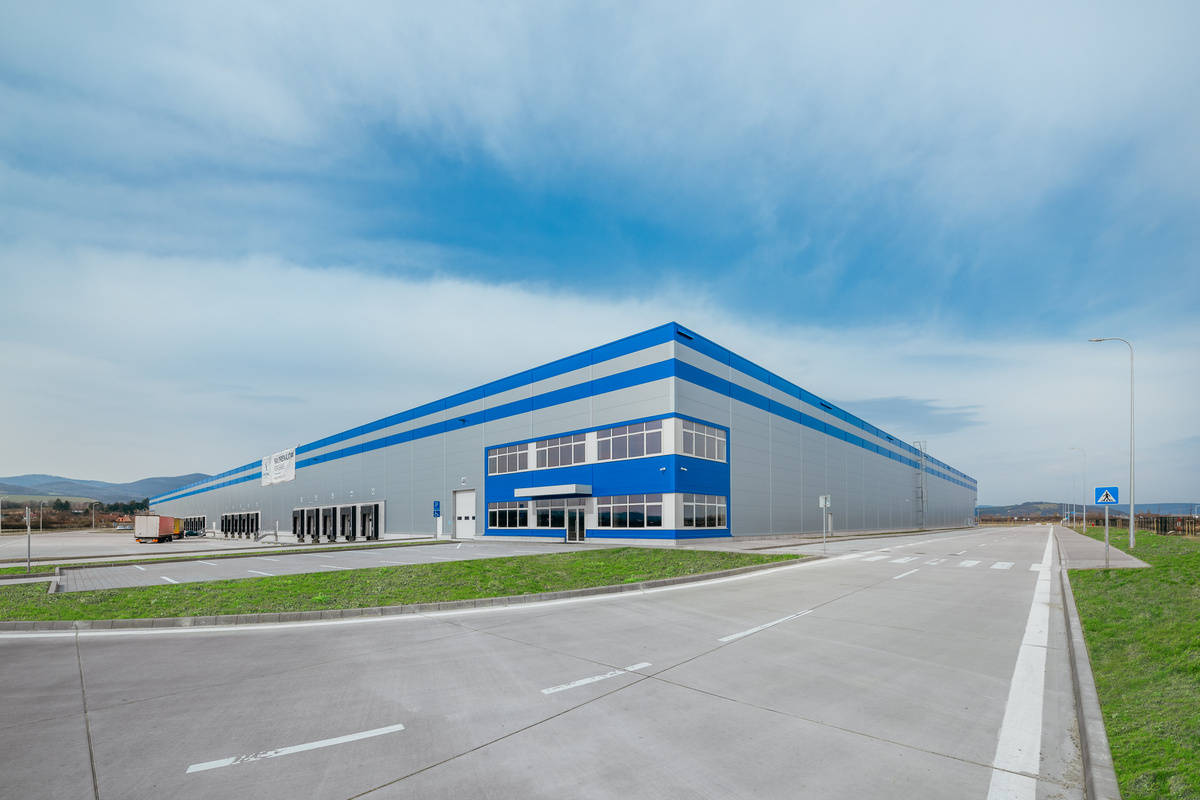 Distribučné centrum s modro-sivým exteriérom a nakladacími dokmi na rozľahlej spevnenej ploche.