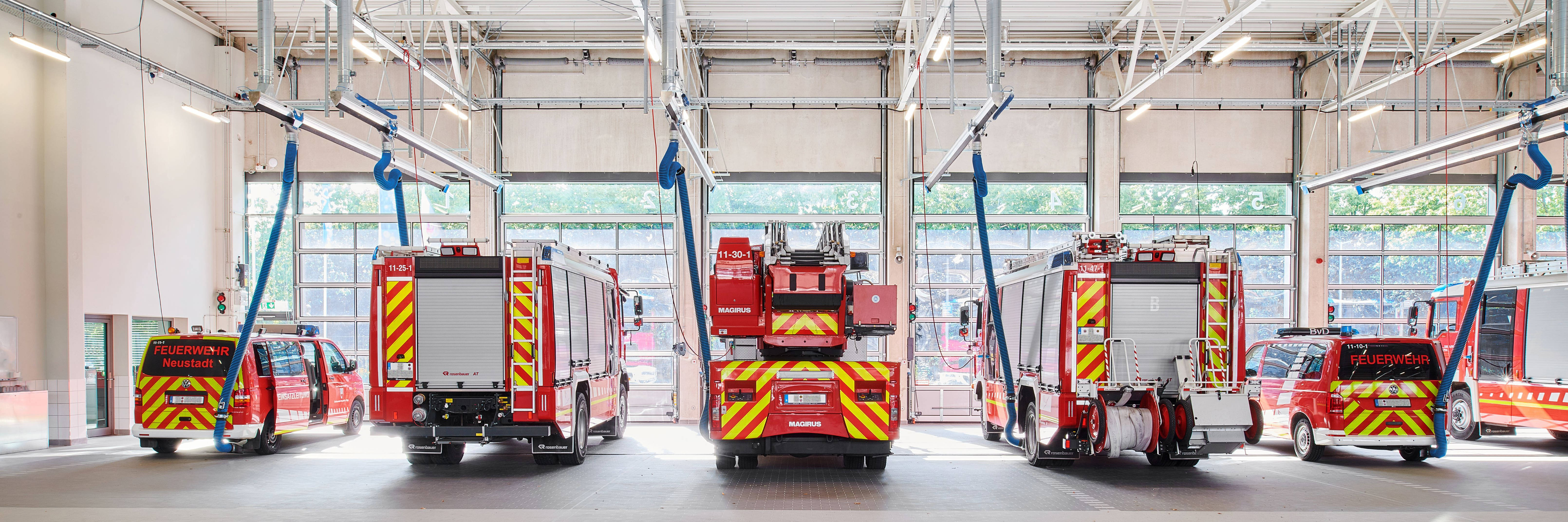 Interior view of a fire station building in which several fire engines are parked.