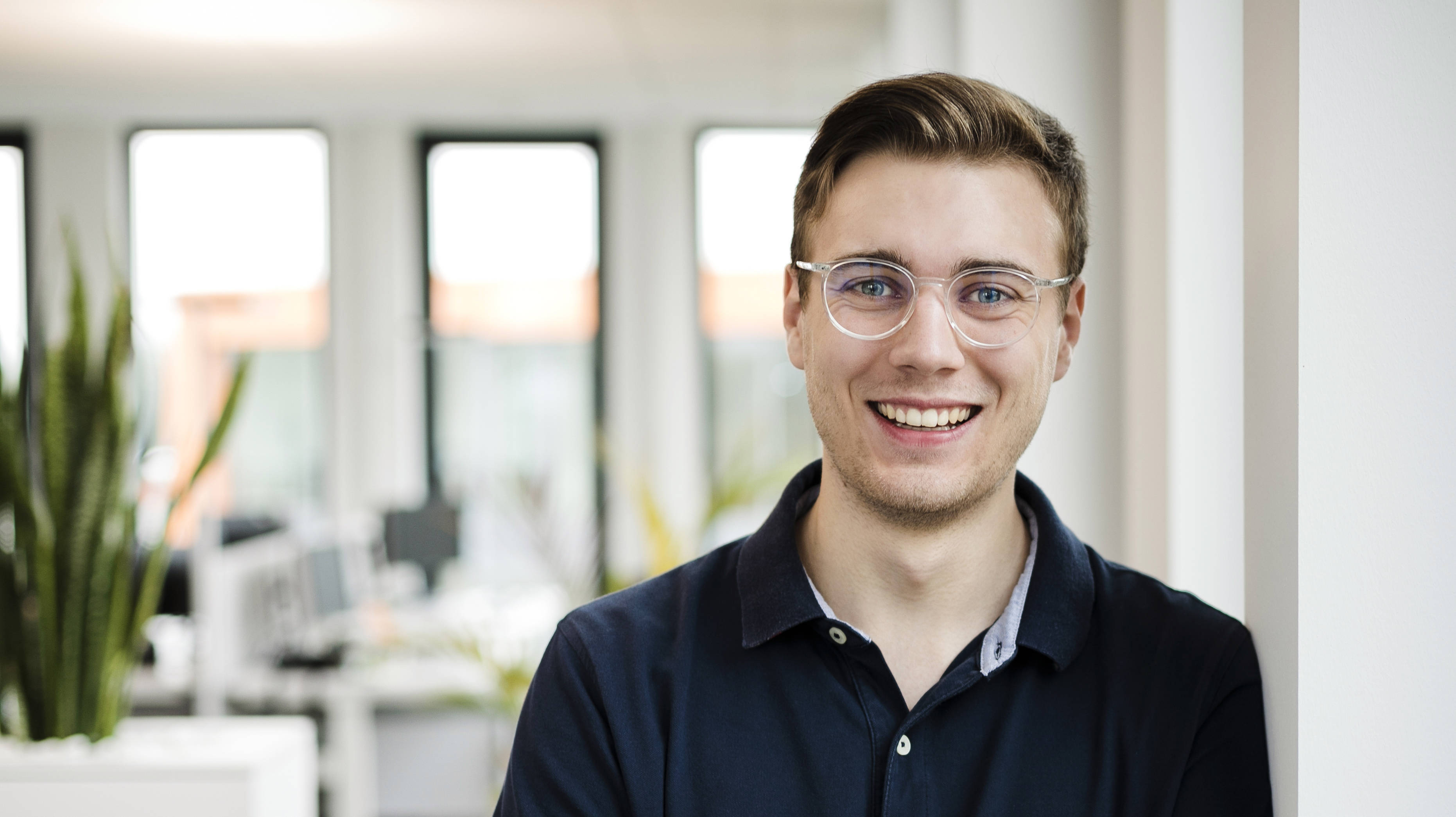 portrait eines jungen mannes mit durchsichtiger brille und verschränkten armen