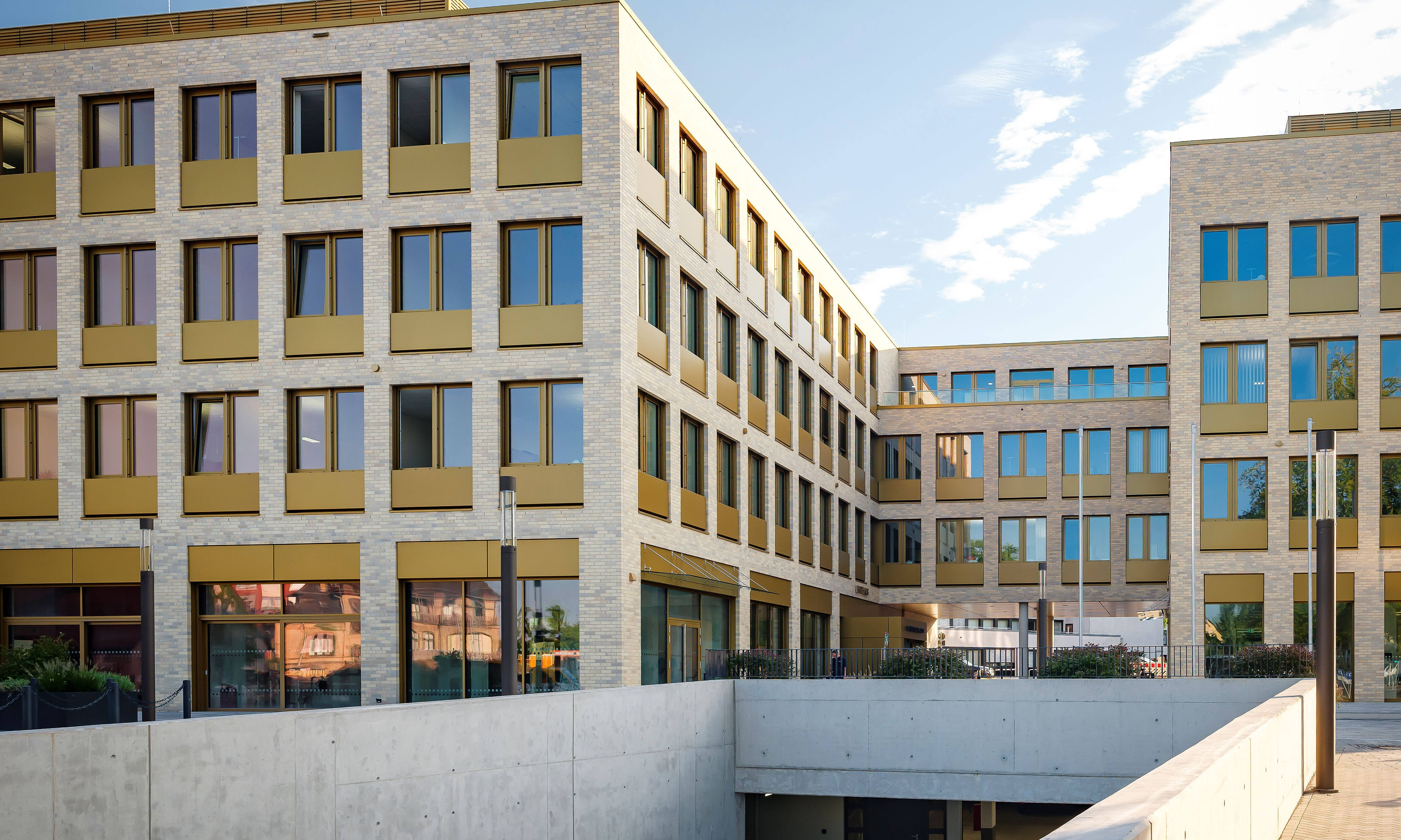 Modernes Bürogebäude mit gelben Fensterrahmen und heller Fassade, flankiert von einem klaren blauen Himmel.