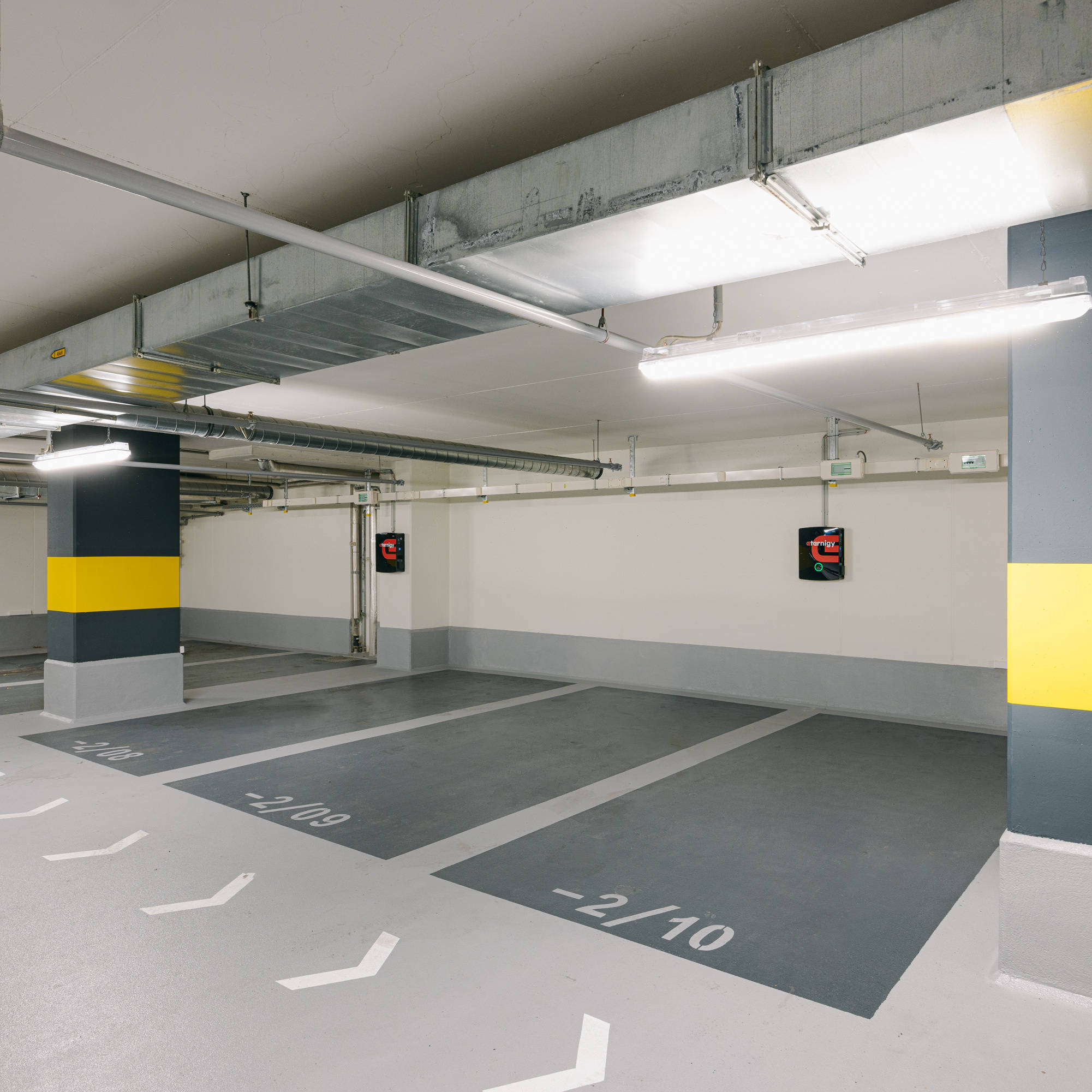 Empty, well-lit underground parking lot with marked parking spaces and yellow stripes on the pillars.