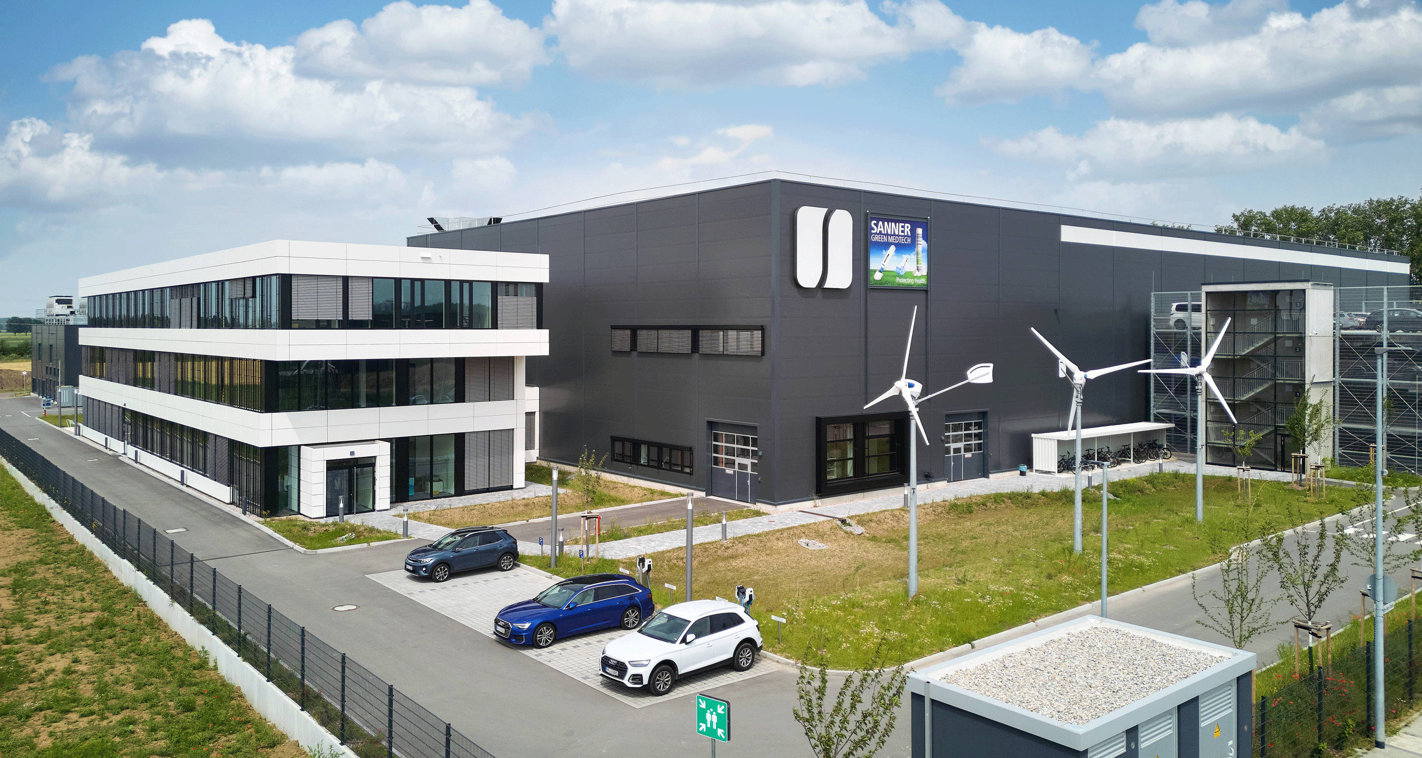 Modern office and industrial building with wind turbines in the foreground, blue sky in the background.