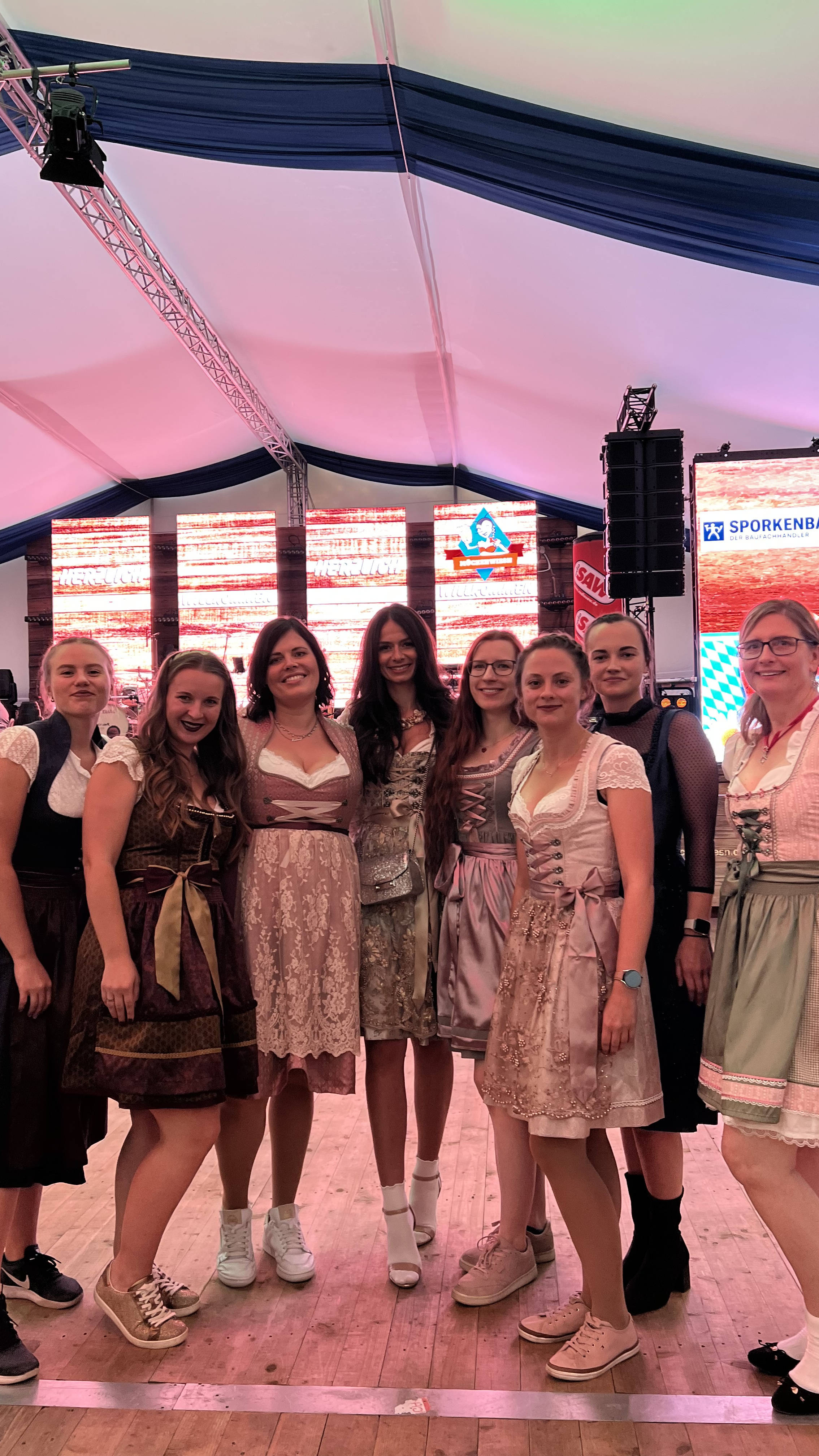 Eine Gruppe von Frauen in Dirndlkleidern steht lächelnd in einem großen Festzelt.