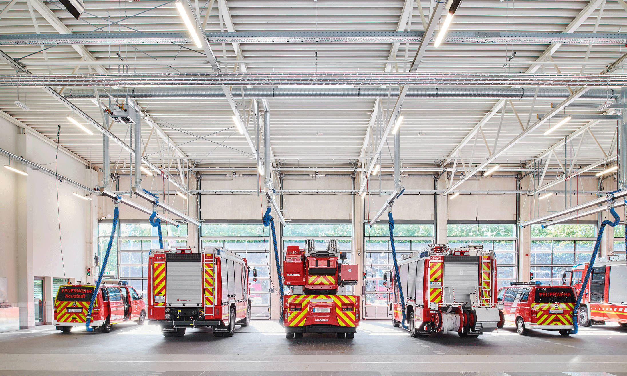 Fire engines park in a modern fire station with open gates and a brightly lit ceiling.