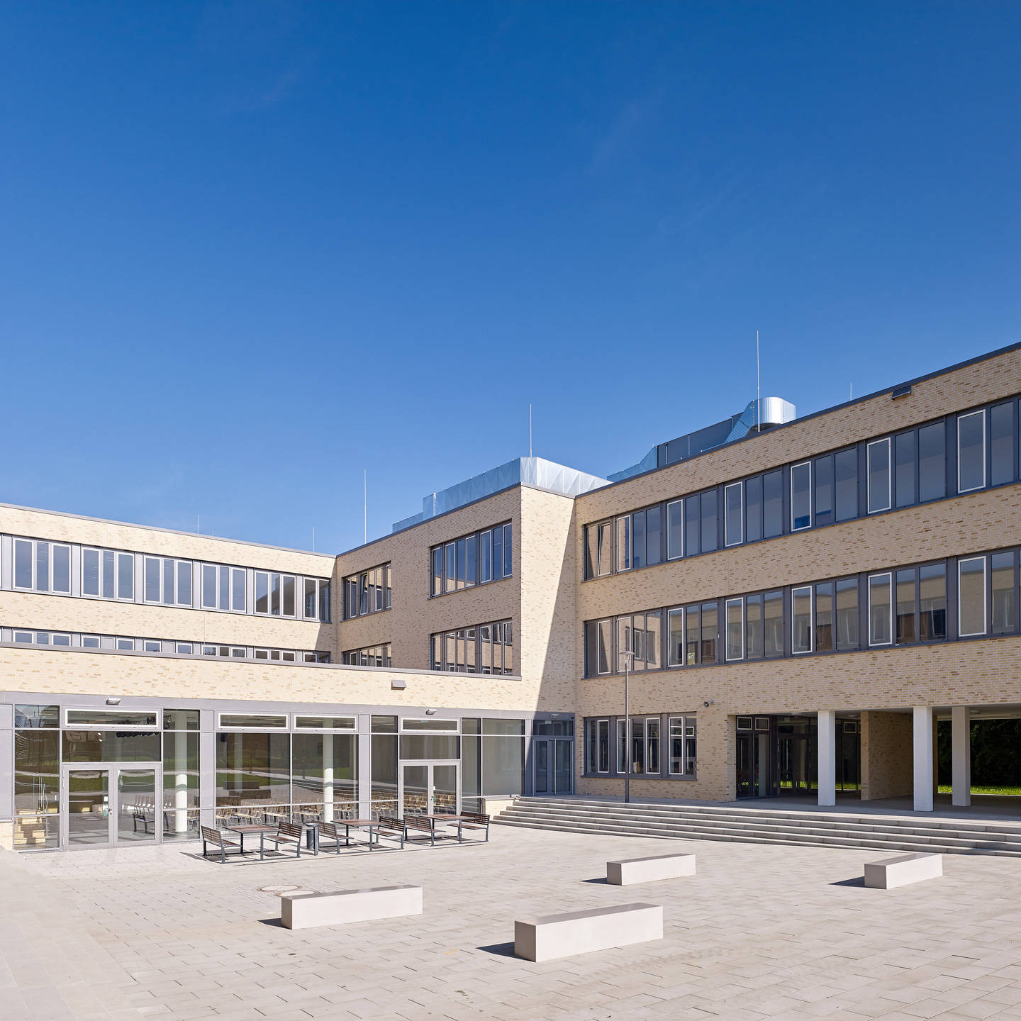 Modern school building with large windows and courtyard under a clear sky.