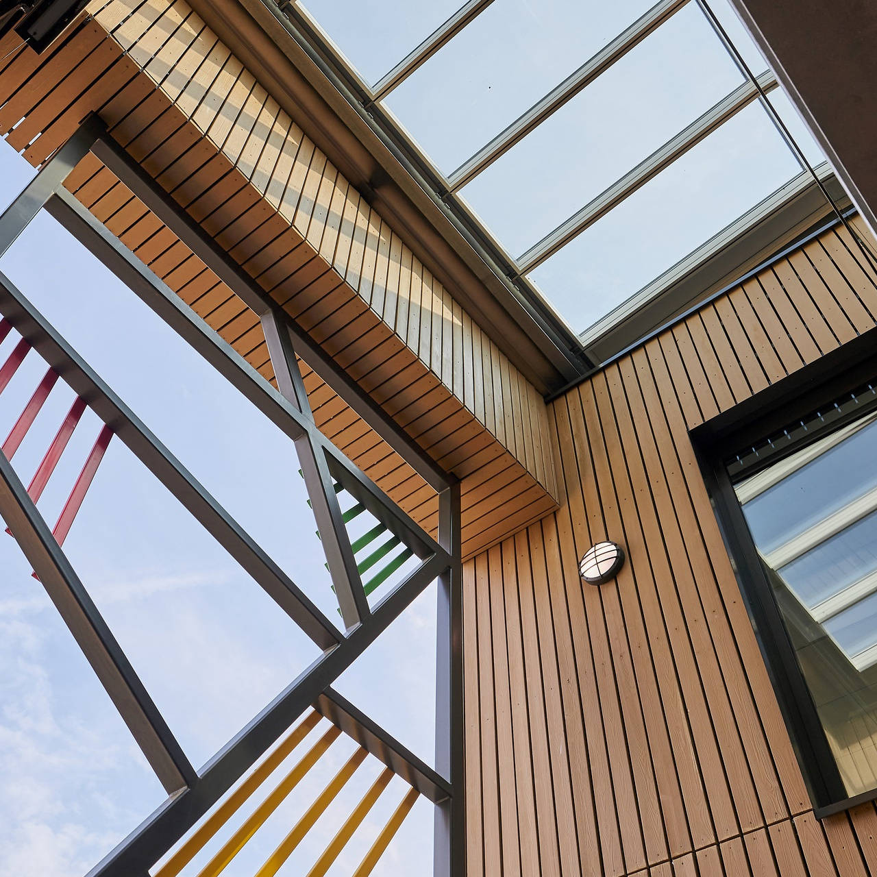 Moderne Architekturansicht von innen, mit farbigen Metallträgern und Holzverkleidung unter einem Glasdach.