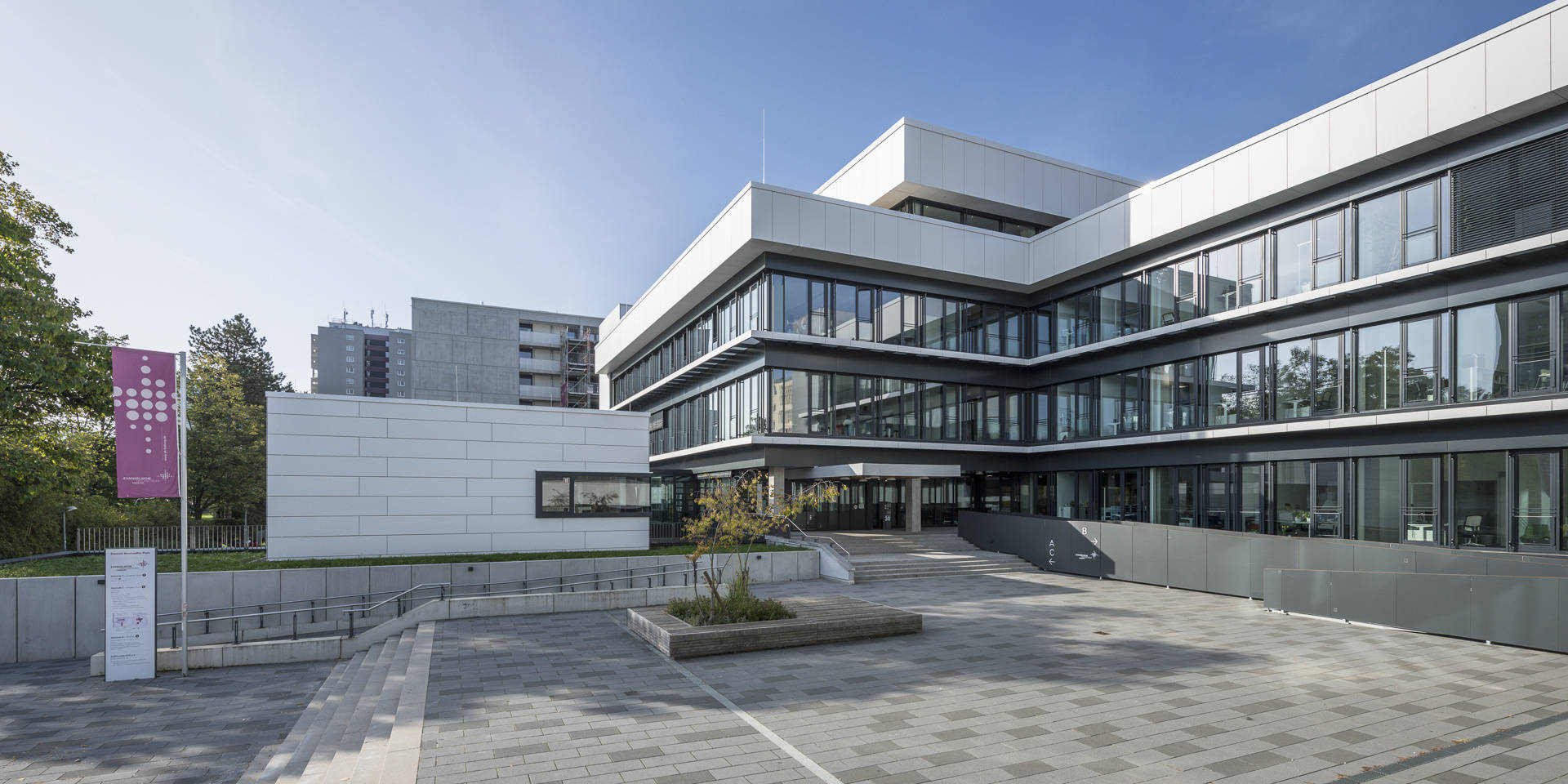 Modernes Bürogebäude mit Glasfassade und gepflastertem Vorplatz an einem sonnigen Tag.